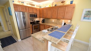 Una cocina con gabinetes de madera, electrodomésticos de acero inoxidable, encimeras de granito y un comedor con sillas blancas.