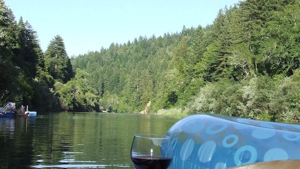 Ein Tretboot auf einem ruhigen Fluss, ein Glas Rotwein und ein Holzruder auf einer gestreiften Matte.