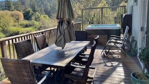 Eine Holzterrasse mit Tisch und Stühlen, einem Whirlpool und Blick auf ein bewaldetes Gebiet.