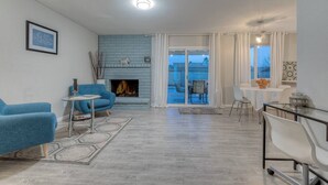 A modern living room with a fireplace, a dining area, and a view of the outdoors. - Fabulous 4 Bedroom Home + Free Private Heated POOL (Glendale)