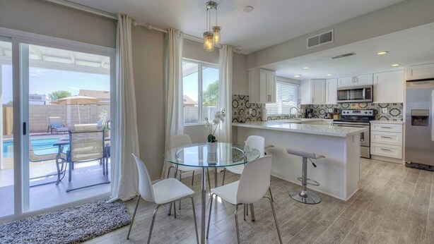 A modern kitchen with a glass dining table, white chairs, and a built-in island. - Fabulous 4 Bedroom Home + Free Private Heated POOL (Glendale)