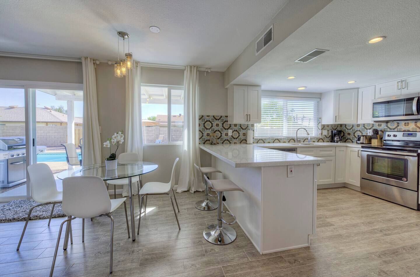 A modern kitchen with white cabinets, a central island, stainless steel appliances, and a dining area with a glass table and white chairs.
