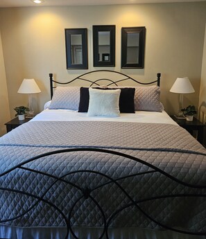 A neatly made bed with a quilted bedspread, two bedside lamps, and three framed mirrors on the wall. - Walk-In Shower/ NEW Decor/ Kings/ CLEAN/ Indoor-Outdoor Pools/ Golf View on 10th (Branson)