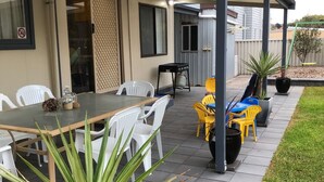 An outdoor patio with a table and chairs, a covered seating area, and potted plants. - Dunes Beach House Goolwa Beach (Goolwa)