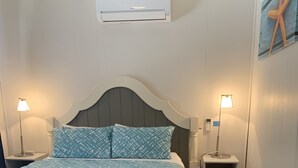 A neatly made bed with a patterned bedspread, two bedside lamps, a small bedside table, and a wall-mounted air conditioner. - Dunes Beach House Goolwa Beach (Goolwa)