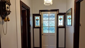 A hallway with a wooden floor, a white door with stained glass windows, and a wall-mounted clock.