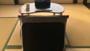 Ein Zimmer mit Tatami-Böden, einem Laptop auf einem kleinen Tisch und einem großen Fenster mit Blick auf die Küste.