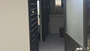 Eine geöffnete Tür, die zu einem kleinen, abgeschlossenen Raum mit einem Fenster und einer Mülltonne führt.