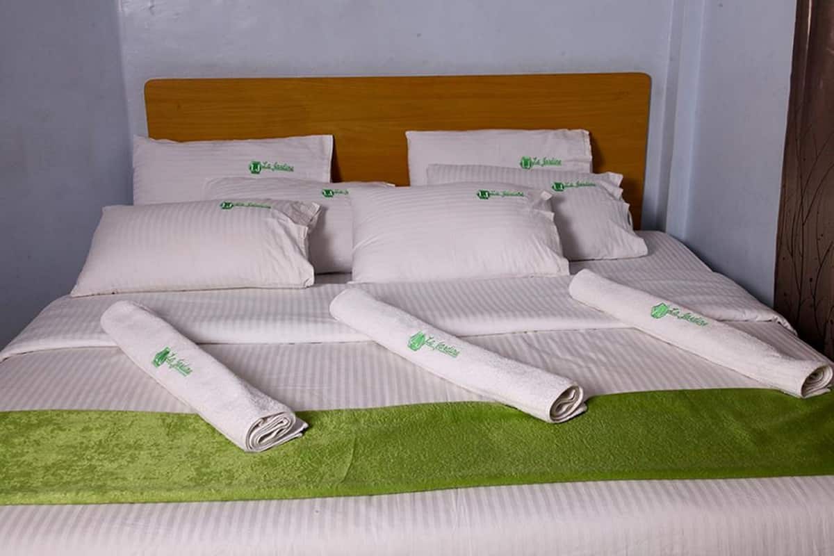 Un lit bien fait, avec du linge de lit blanc et des serviettes vertes, une tête de lit en bois et un plaid vert.