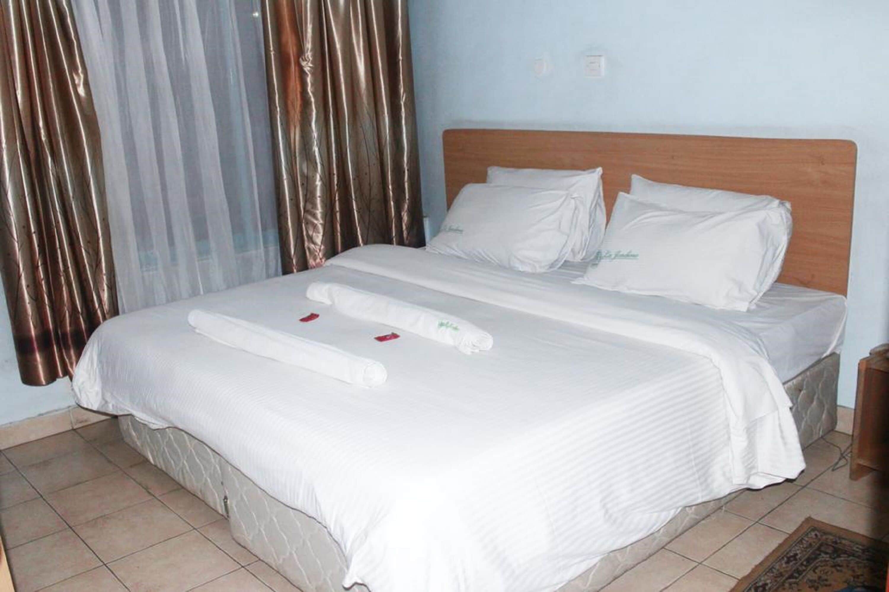 A neatly made bed with white linens and towels, a wooden headboard, and a curtain partially drawn to the side.