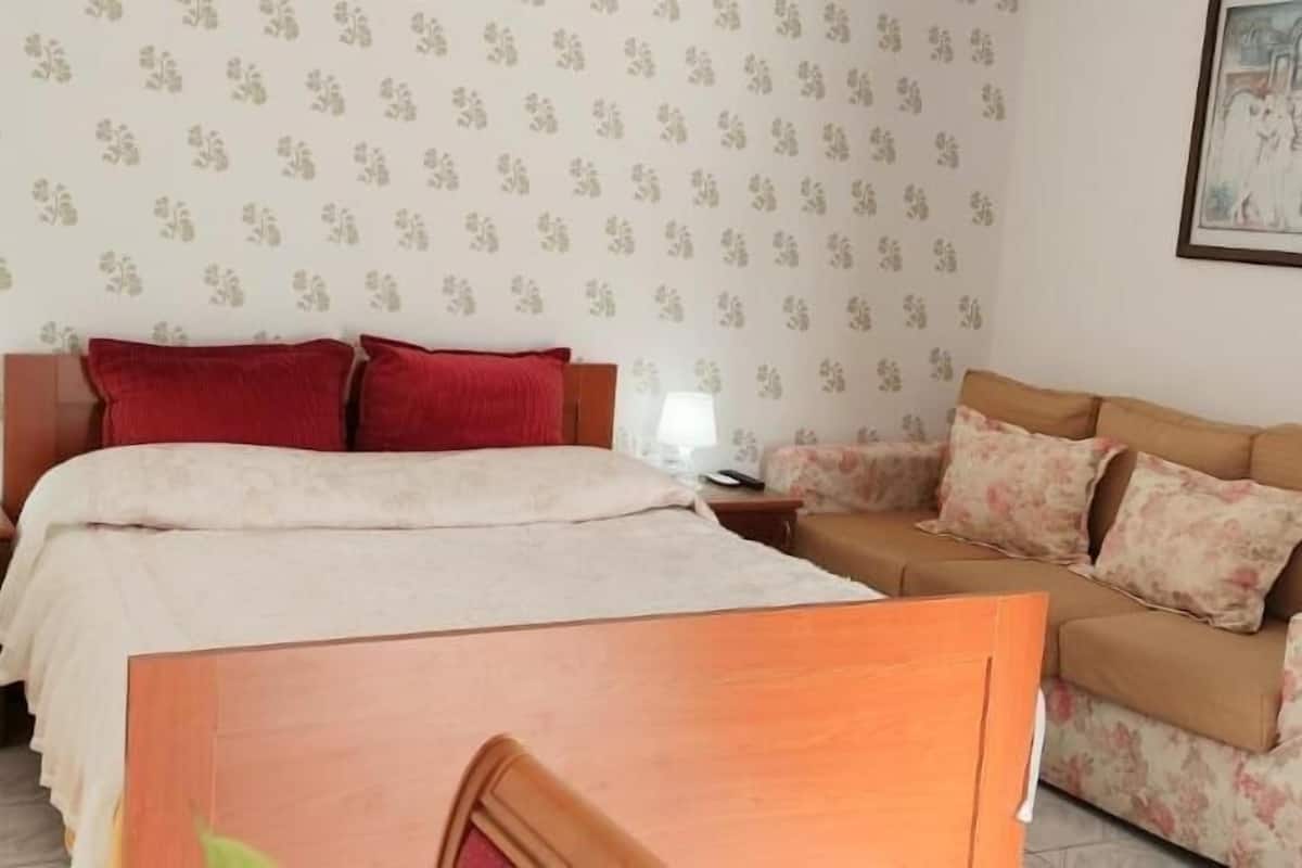 Un dormitorio con cama, mesita de noche, sofá y una pared con estampado floral.