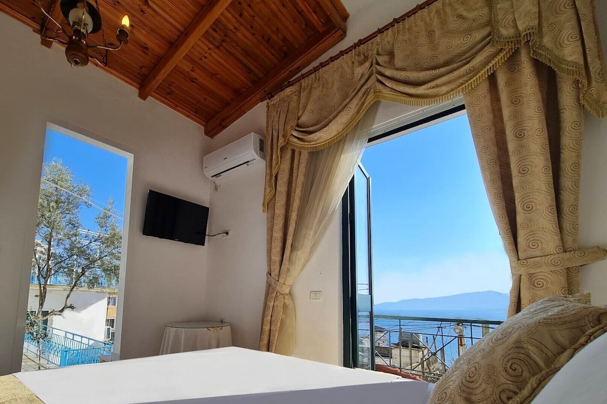 A bedroom with a bed, a TV, an air conditioning unit, and a view of the sea.