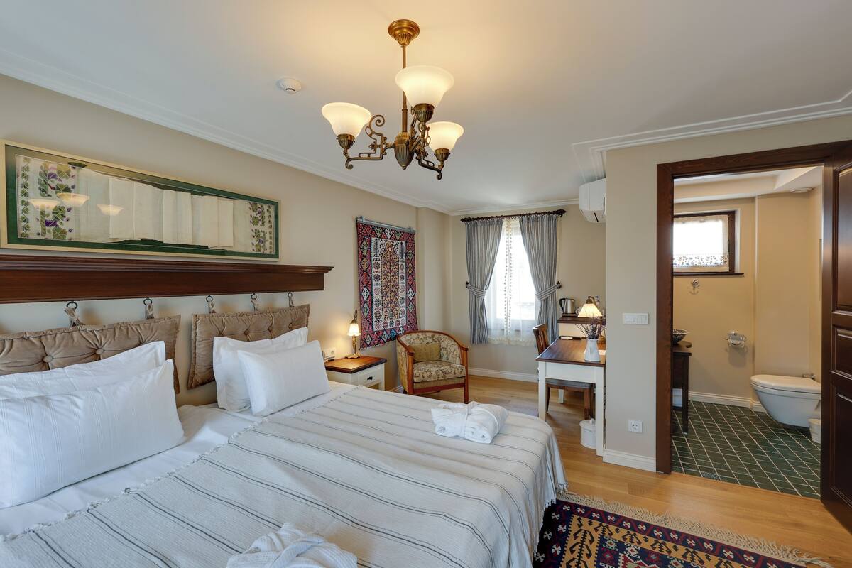 A hotel room with a large bed, a chair, a desk, and a bathroom visible through an open door.