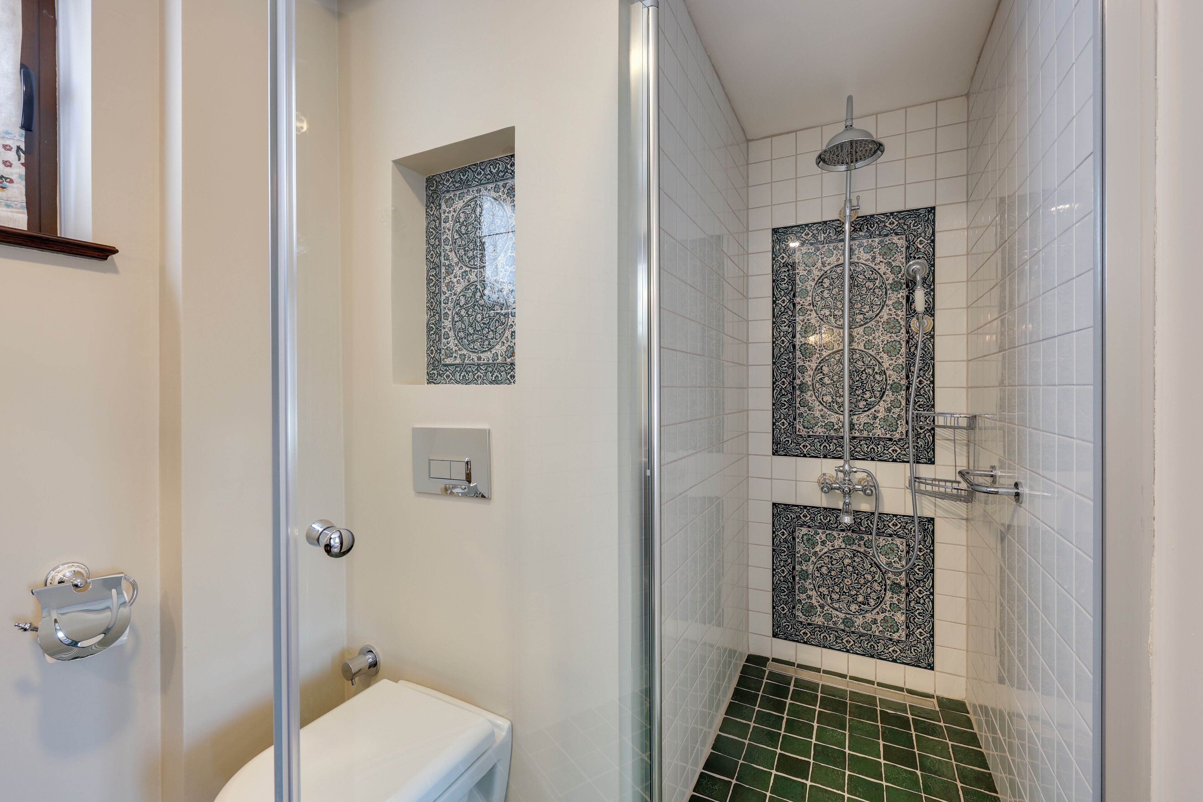 A bathroom with a glass-enclosed shower, a toilet, and decorative tiles.
