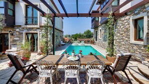 Un espace aménagé au bord de la piscine, avec une table et des chaises en bois, des murs en pierre et une vue sur la piscine.