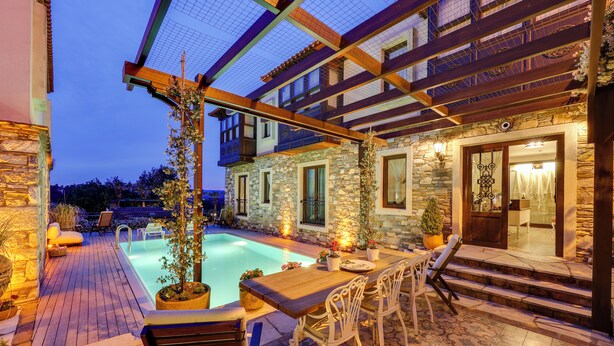 Un espace aménagé au bord de la piscine, avec une terrasse en bois, des murs en pierre et une piscine en pierre. On y trouve des espaces de détente en plein air et une pergola.