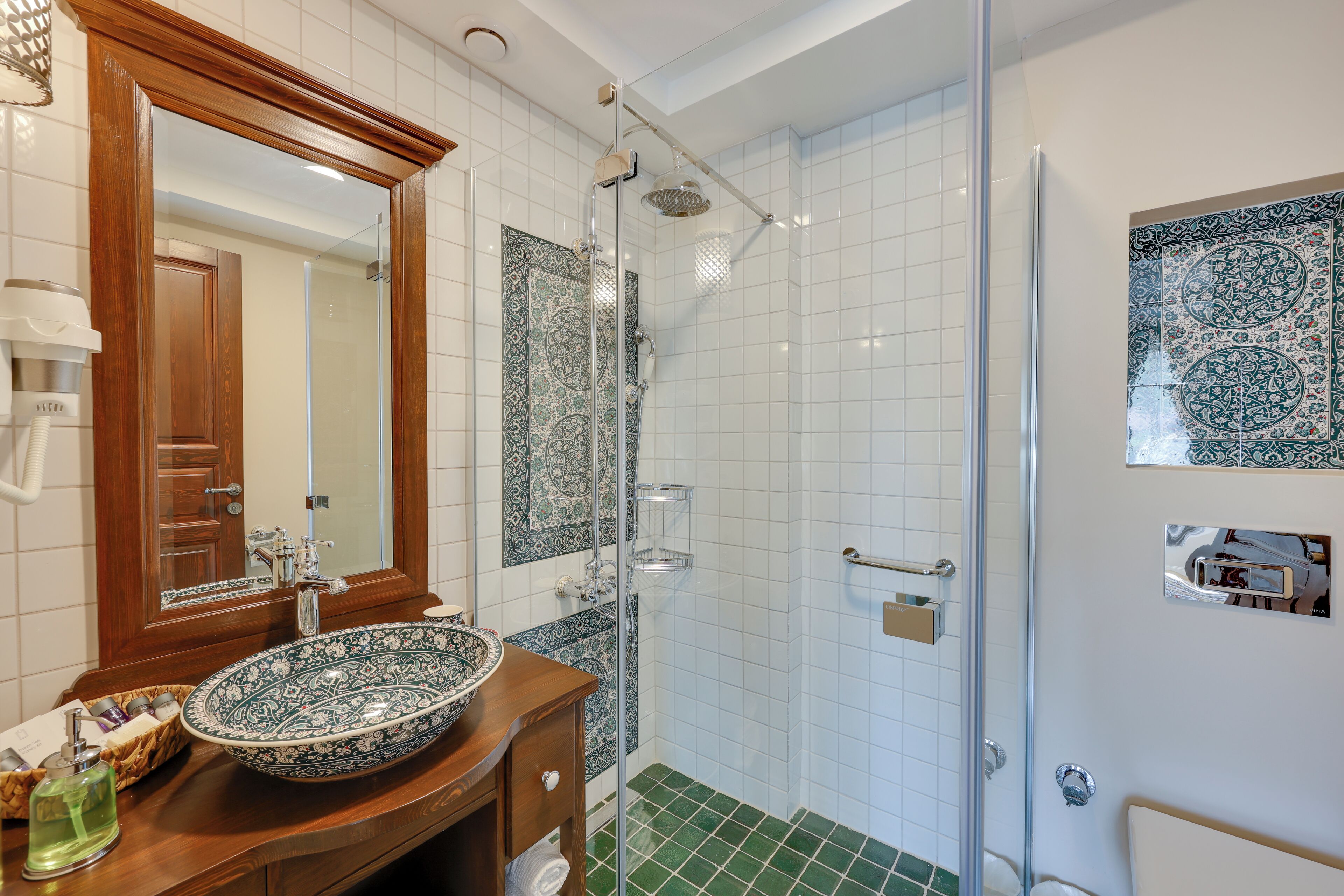 A bathroom with a large mirror, a bowl sink, a shower, and patterned tiles.