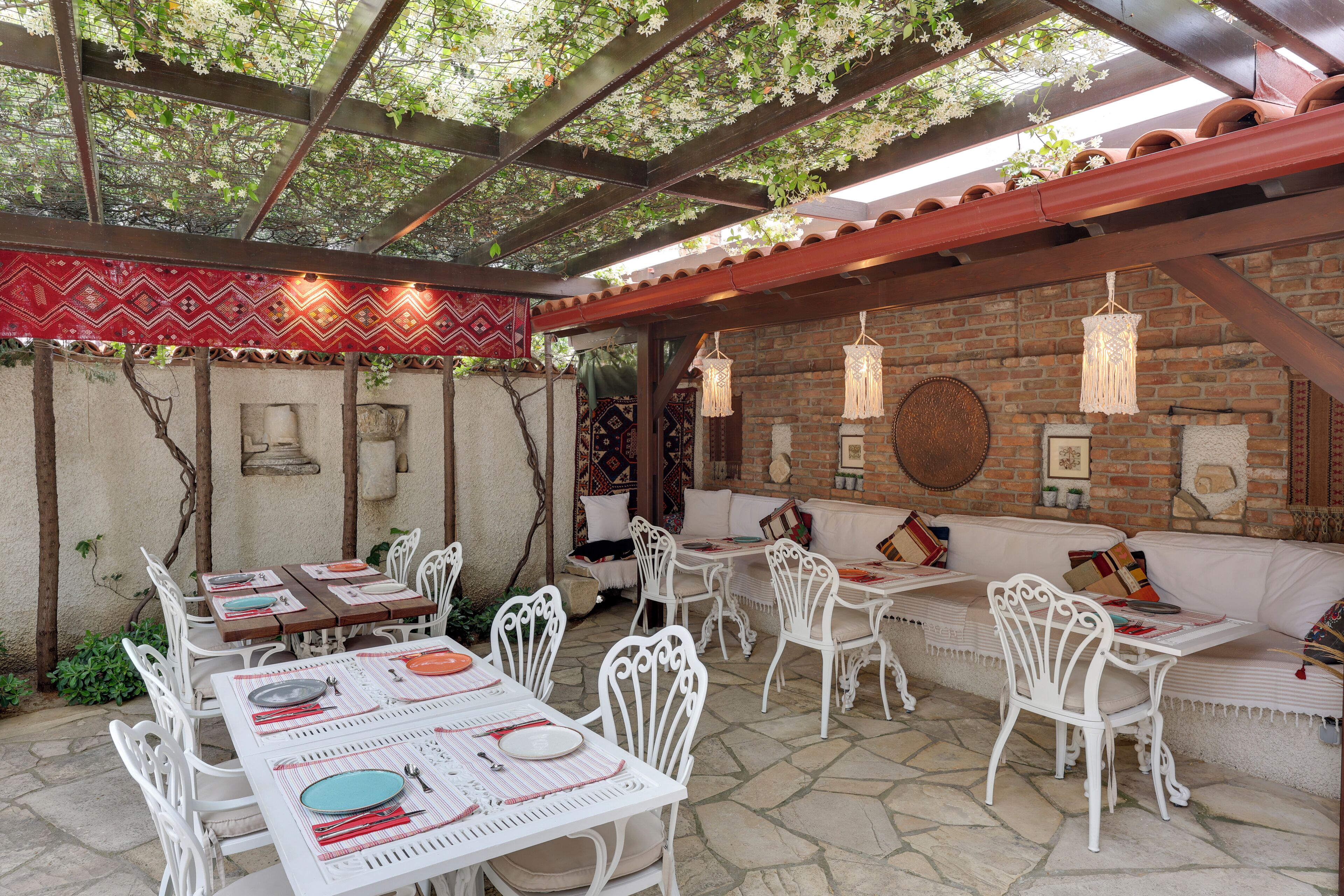 An outdoor patio with white metal tables and chairs, a brick wall, and hanging light fixtures.