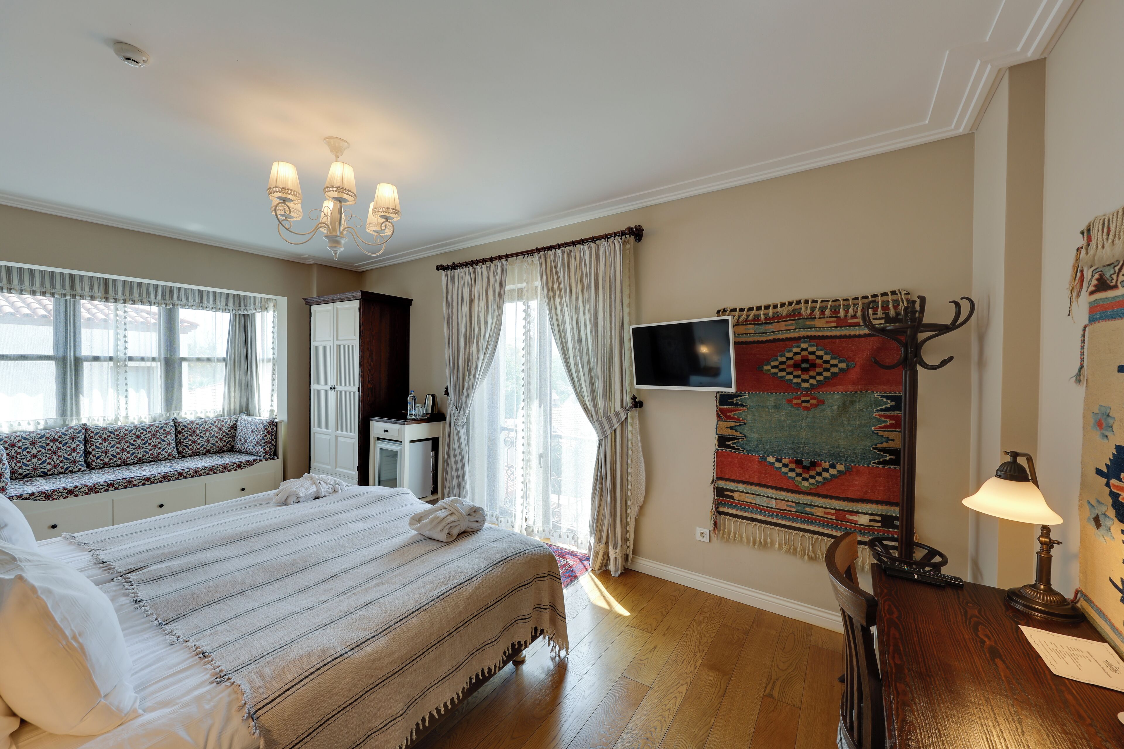 A bedroom with a large bed, a television, a desk with a lamp, and a window with curtains.