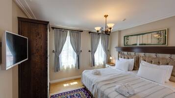 A hotel room with a bed, a television, a wooden wardrobe, a chandelier, and a patterned rug.