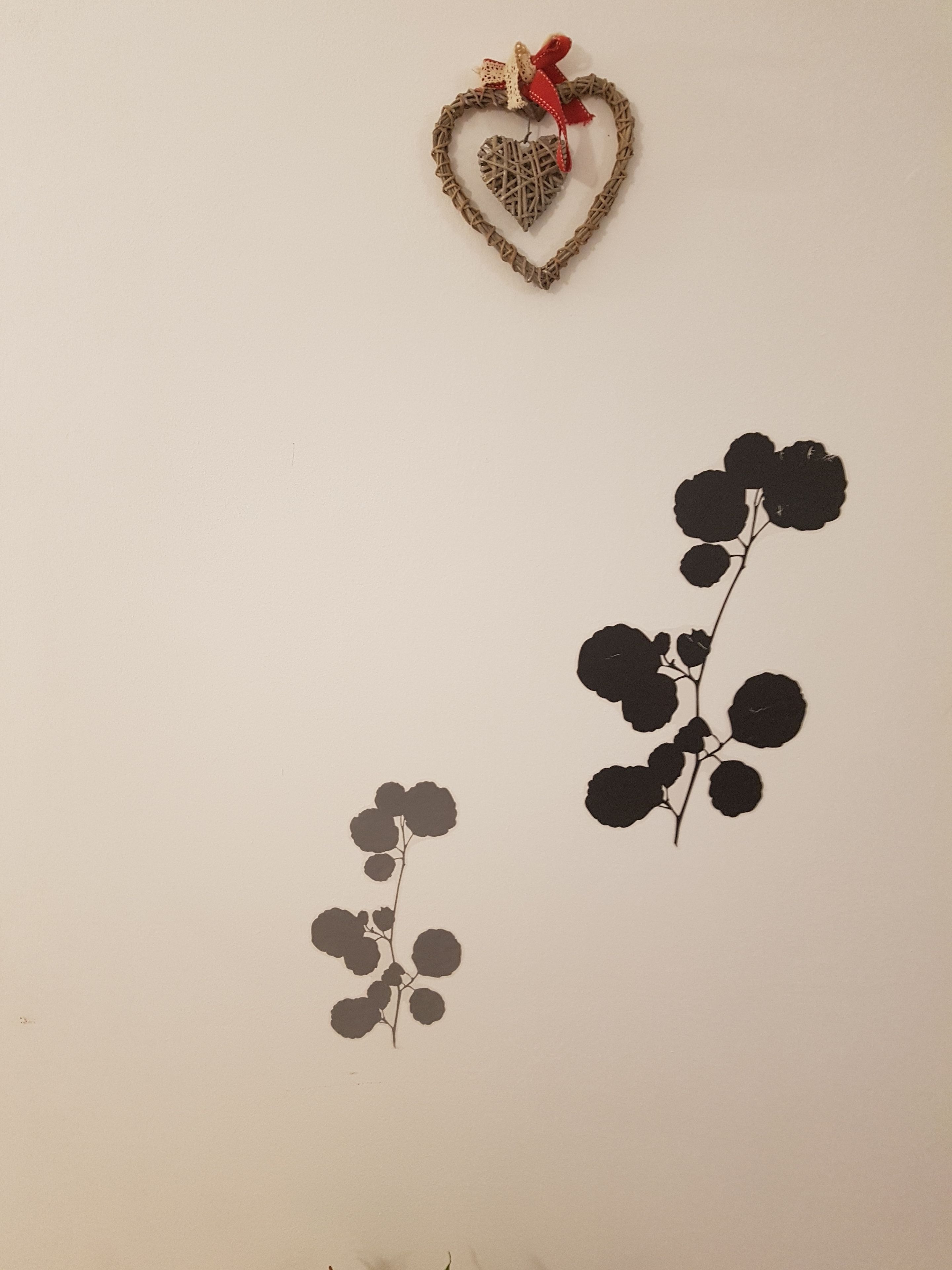 A wall with a heart-shaped decoration and two black floral wall art pieces.