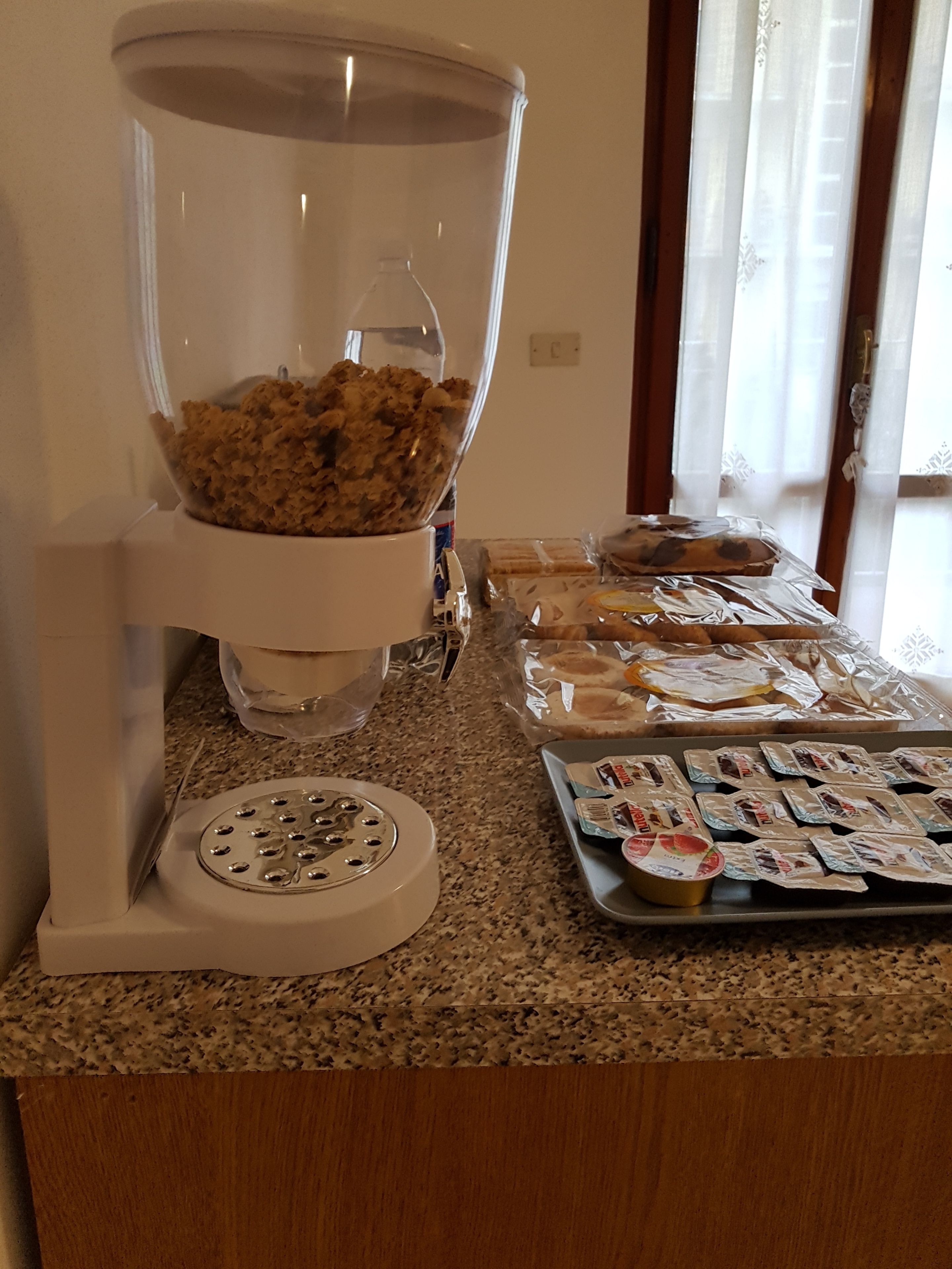 Une cuisine équipée d’un mixeur, d’un plan de travail sur lequel sont posés des aliments emballés, et d’une fenêtre avec des rideaux.