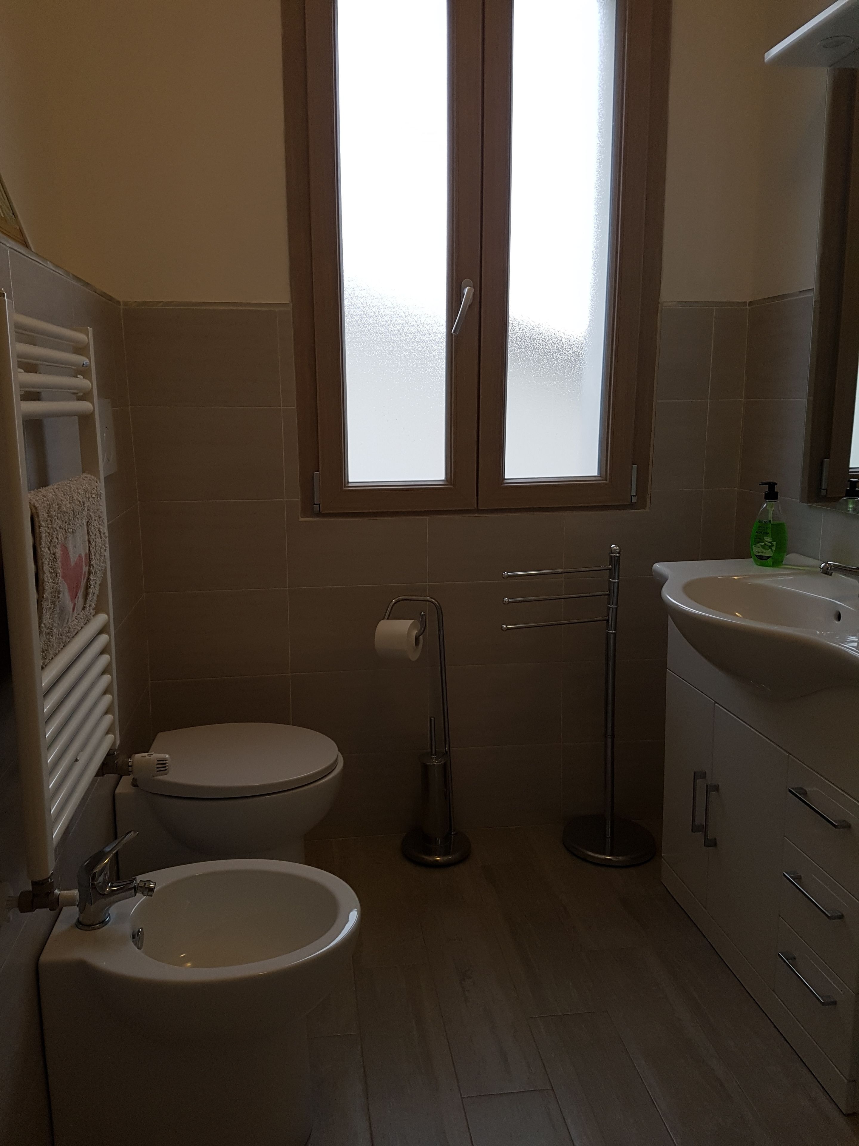 A bathroom with a toilet, bidet, sink, and a window with frosted glass.