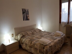 A bedroom with a bed, bedside tables, a nightstand, a radiator, and a window with curtains. - B&B Buscemi (Pistoia)