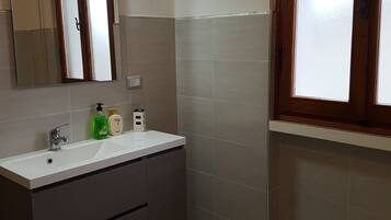 Un bagno con un lavandino bianco, mobili scuri, uno specchio e una finestra con vetro satinato.