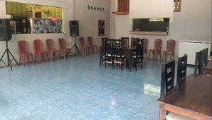 Una habitación con piso de baldosas, un escenario con un orador y un comedor con mesas y sillas.