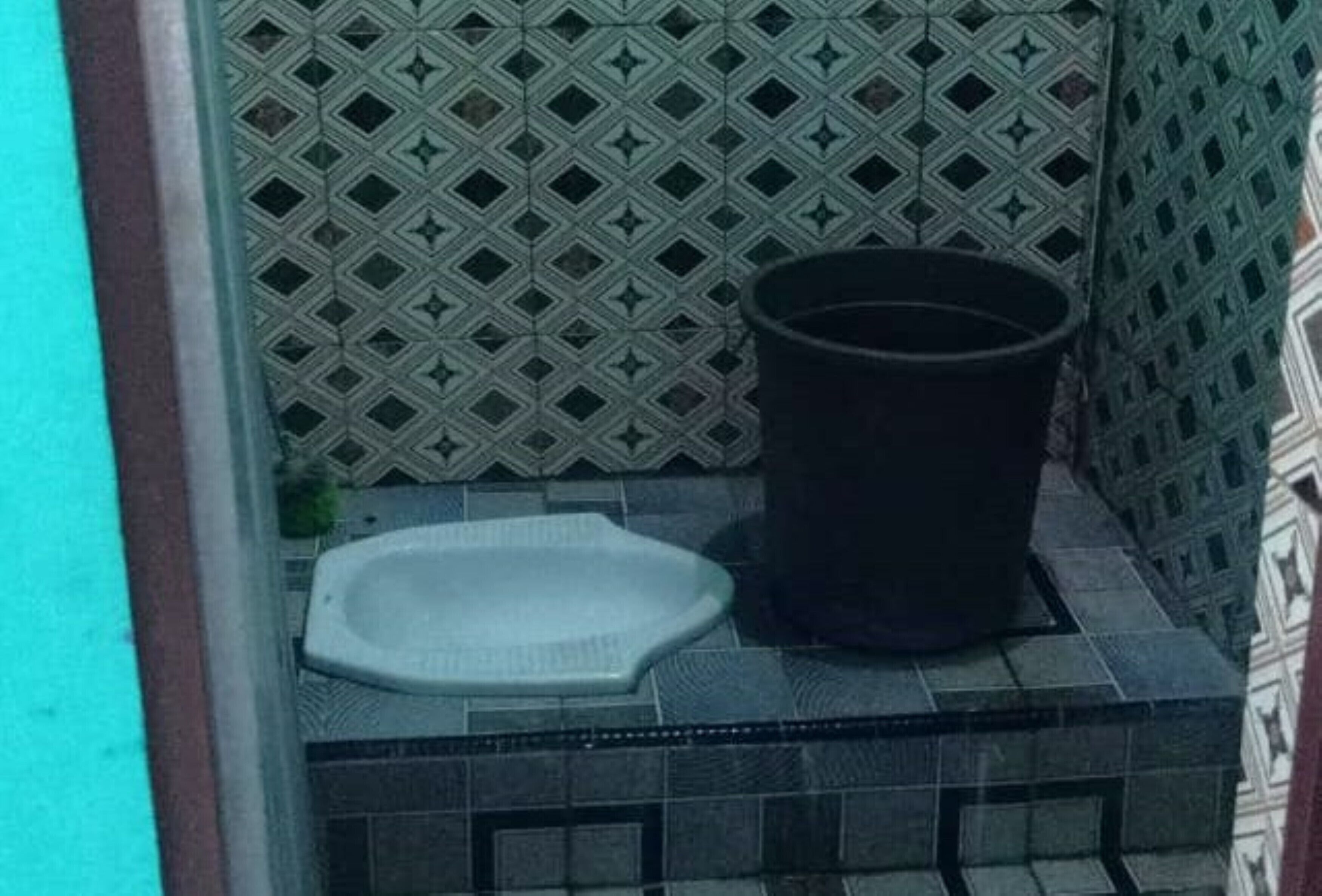 Un baño pequeño con pared estampada, inodoro blanco y un bote de basura negro.