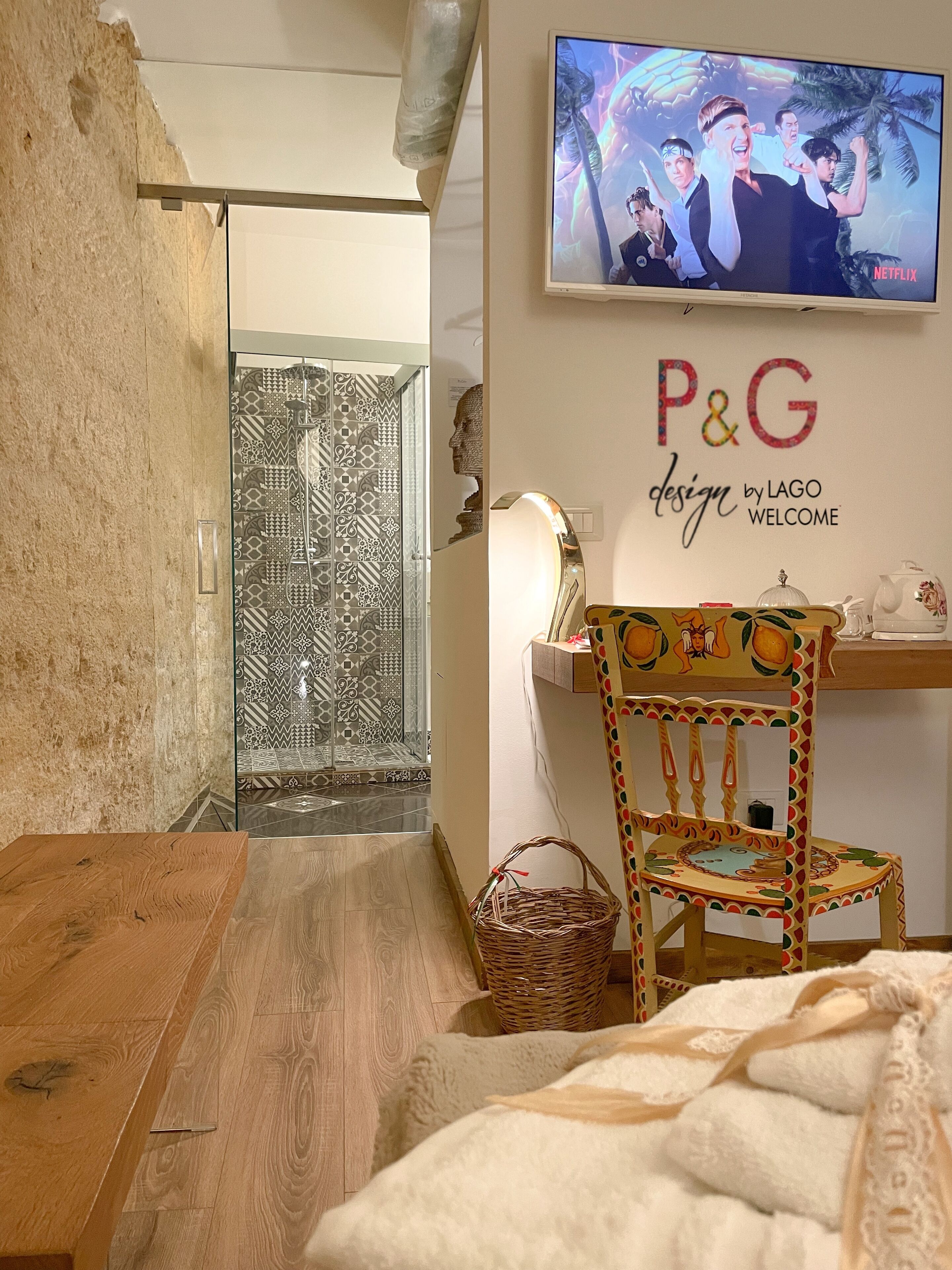 Une chambre d’hôtel moderne avec un plancher en bois, un lit, une télévision, un mur orné d’un logo au design P&G, et une zone de douche décorée de motifs.