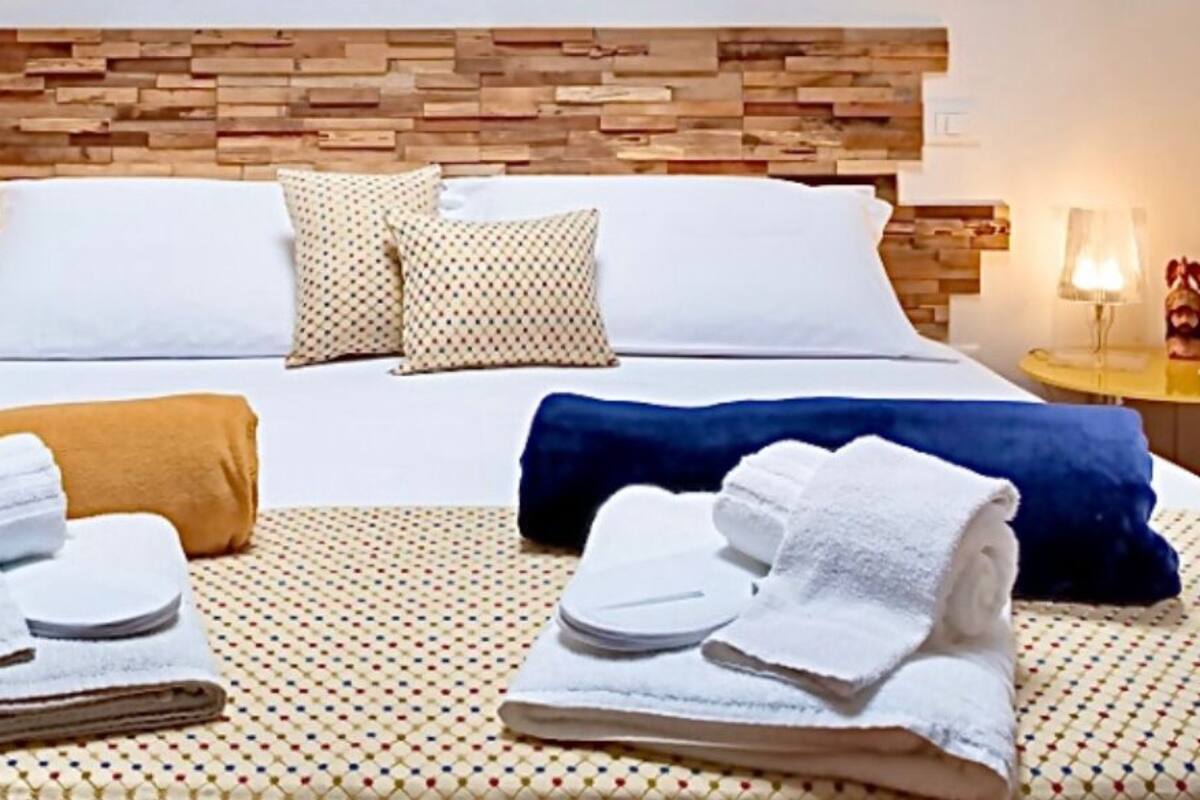 Ein Hotelzimmer mit einem Holzkopfende, einem Bett mit weißer Bettwäsche, zwei Nachttischen mit Lampen und Handtüchern auf dem Bett.