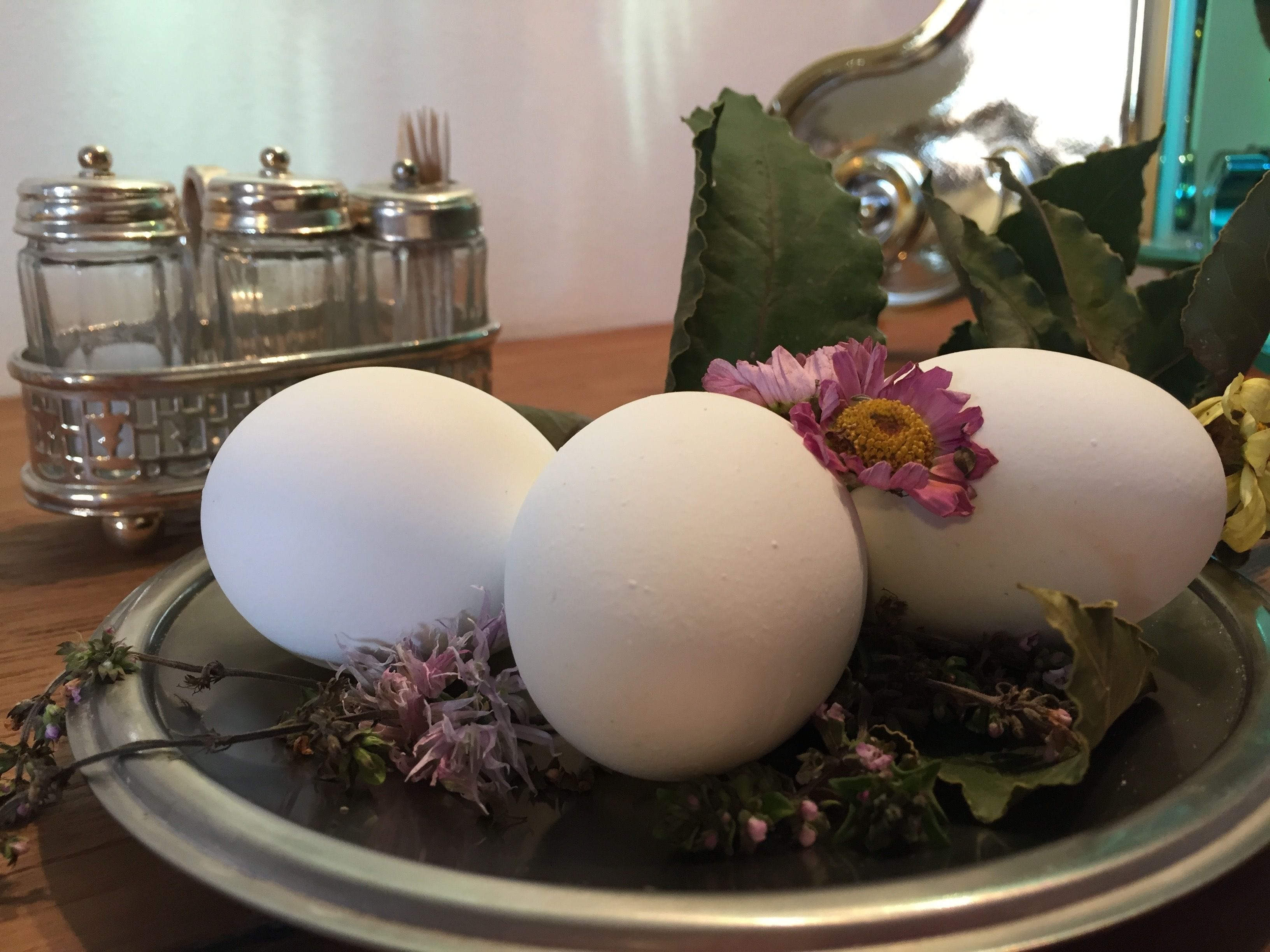 Tres huevos blancos en un plato con flores y hierbas.