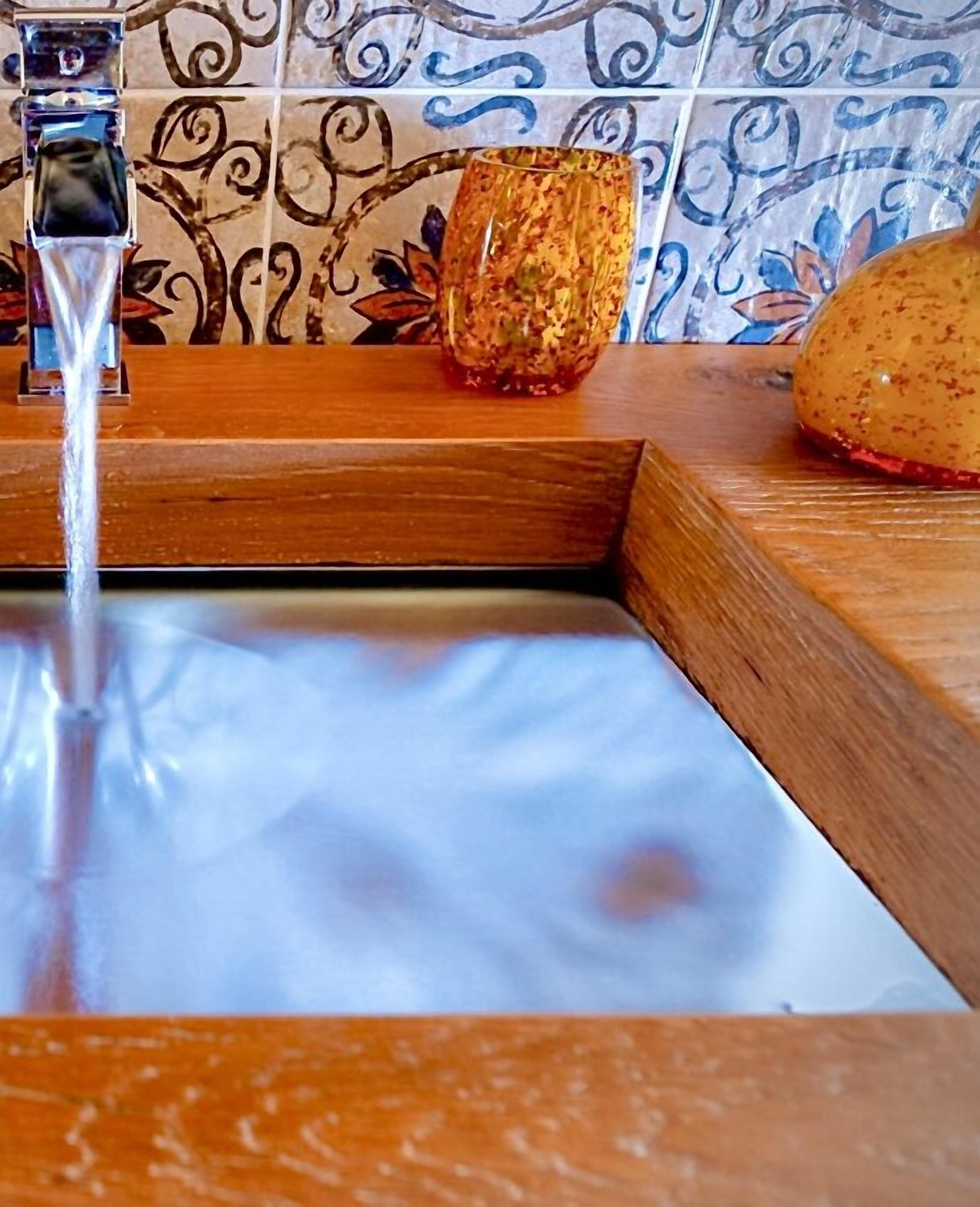 A bathroom with a wooden sink, a glass container, and a decorative tile backsplash.