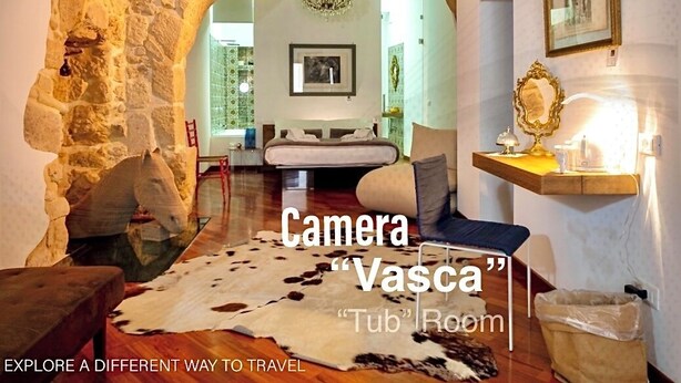 Una habitación con un arco de piedra, una araña, una cama y un tapiz de cuero de vaca.