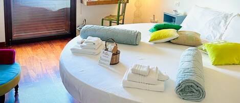 A round bed with neatly folded towels, a bedside table with a lamp, and a view of the sea through a sliding door.