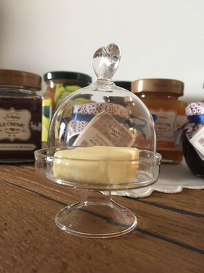 A glass-covered butter dish on a wooden table with jars of condiments in the background.