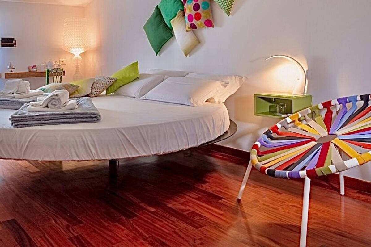 Ein Schlafzimmer mit einem runden Bett, einem bunten Sessel und einem Nachttisch mit Lampe.