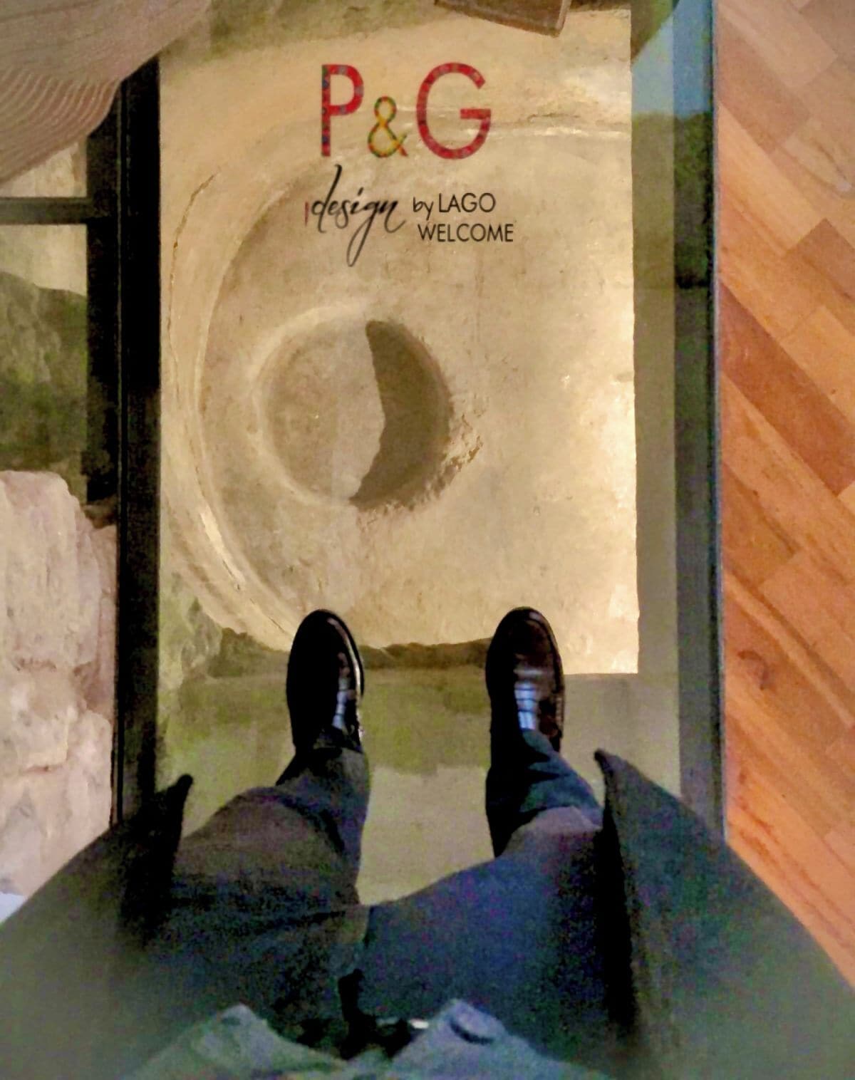 Una persona sentada en un banco con un cartel grande al fondo que dice “P&G design by LAGO WELCOME”.