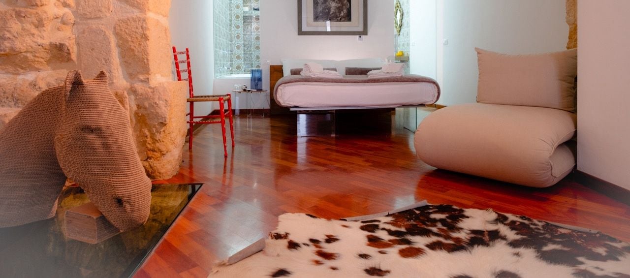A modern bedroom with a stone wall, a chandelier, a bed, a red chair, and a cowhide rug.