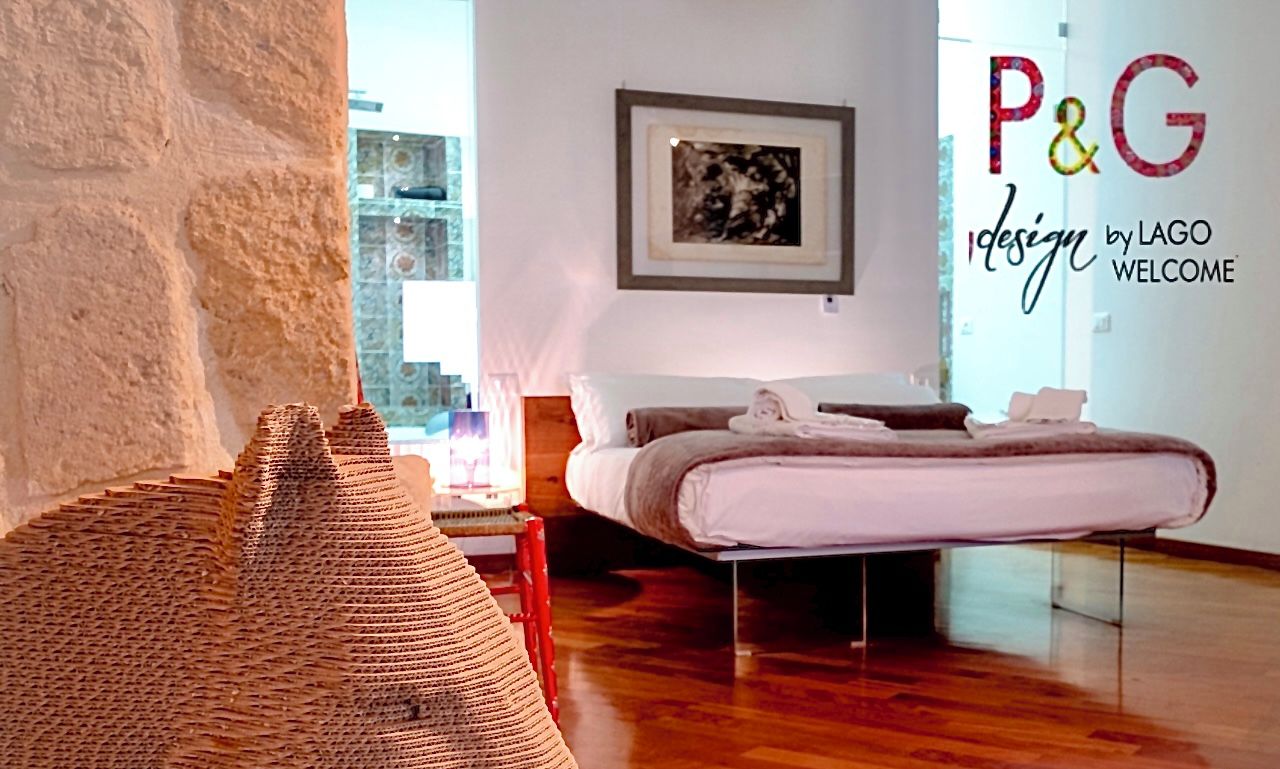 A room with a large, textured sculpture resembling a horse's head on a wooden base, a bed with a white mattress and pillows, a framed picture on the wall, and a wooden floor.