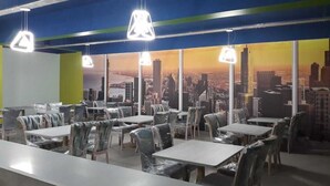 Ein Restaurant mit Tischen und Stühlen, einer Stadtkulissen-Mural an der Wand und hängenden Pendelleuchten.