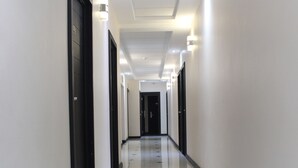 Ein langer, schmaler Korridor mit weißen Wänden und schwarzen Türen, der zu einem dunklen Raum am Ende führt.
