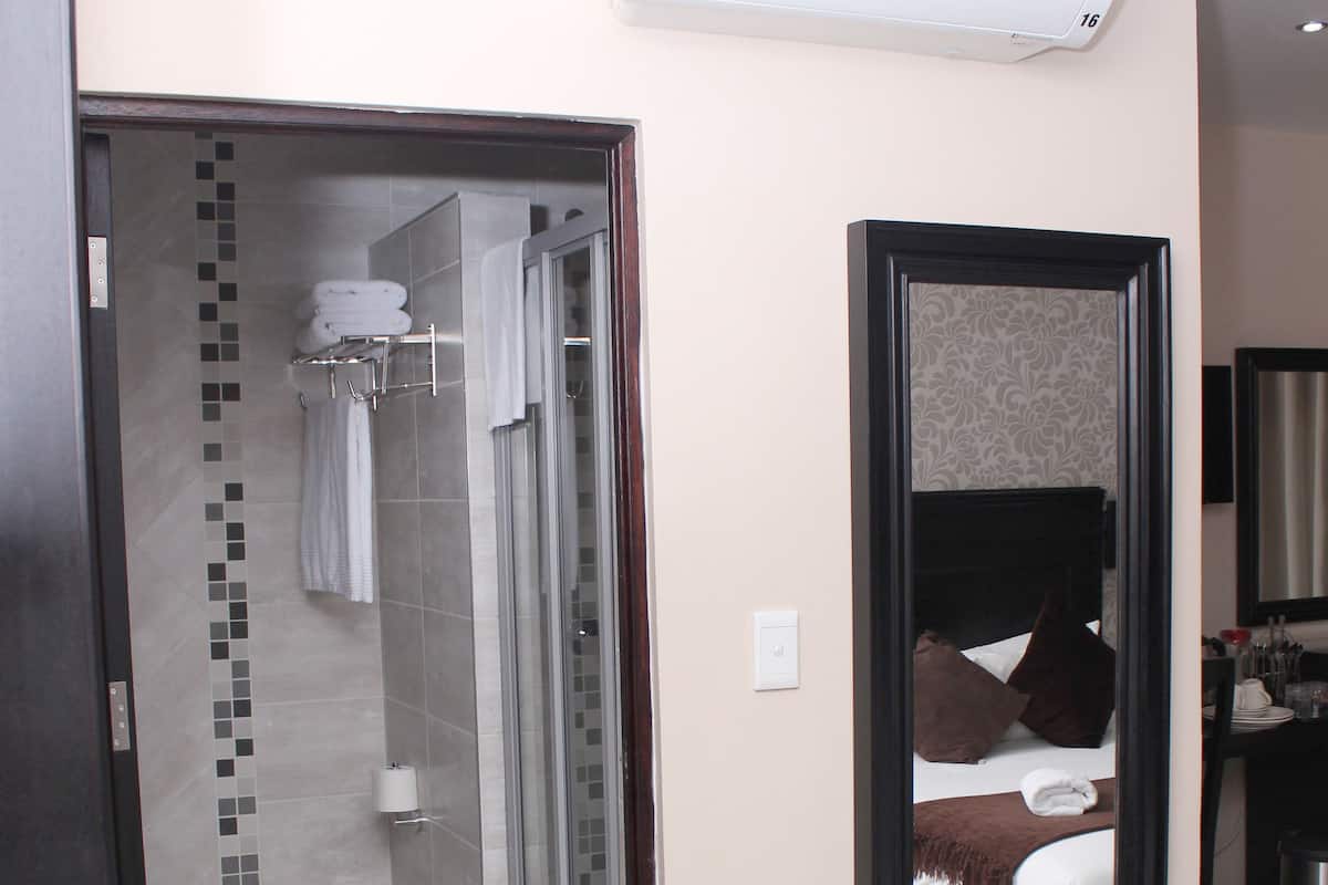 Une chambre d’hôtel avec une douche, un lit doté d’une tête de lit marron, un miroir et un coin repas avec une chaise.