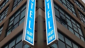Ein Hotel mit zwei vertikalen Schildern, auf denen 'HOTEL' und 'GALAXY TOWER' steht, an der Gebäudeecke.