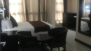 Ein Hotelzimmer mit einem Bett, einem Schreibtisch, zwei Stühlen, einem Spiegel und Vorhängen.