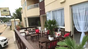 Una terraza de madera con mobiliario exterior, una planta en maceta y un edificio con balcón.