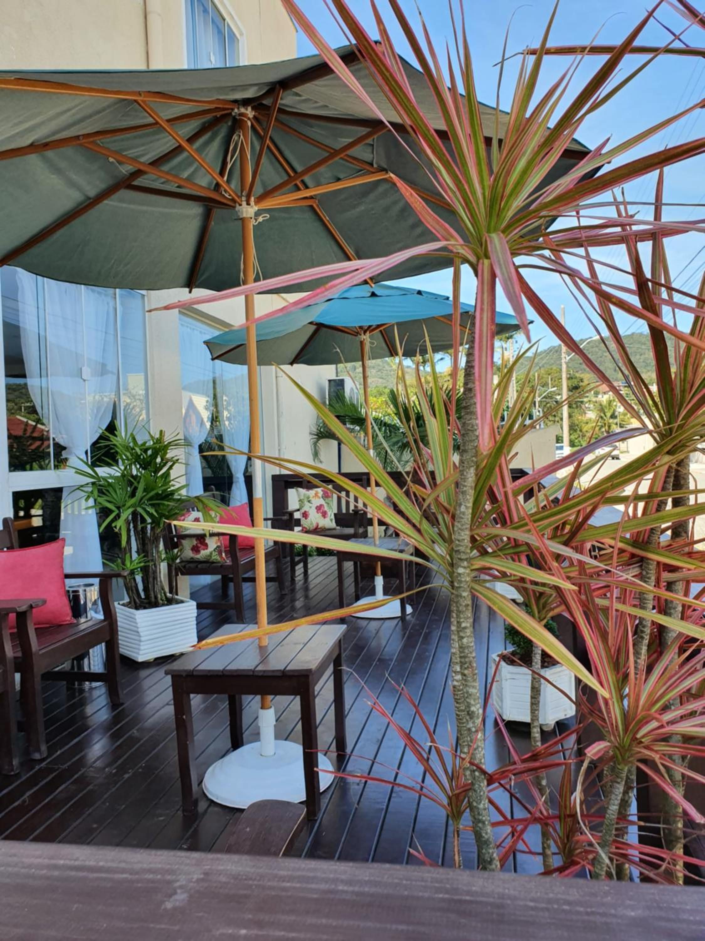 Eine Terrasse im Freien mit Holzboden, Tischen, Stühlen und Sonnenschirmen als Sonnenschutz.
