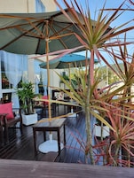 Un patio al aire libre con piso de madera, mesas, sillas y sombrillas para dar sombra.